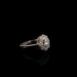 A French platinum and diamond flower ring. Central old cut 5.5mm claw set diamond with a surround of