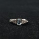 An 18ct white gold aquamarine and diamond art deco style ring. Central square cut aquamarine with