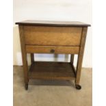 A mid century oak sewing cabinet with lift up lid and drawer on casters.
