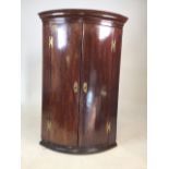 A bow fronted mahogany veneered corner cupboard with double doors to three shelves. W:69cm x D: