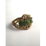 A yellow metal dress ring set with three nephrite cabochons. Size P. 5.2g.