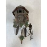 A Black Forest style cuckoo clock with bird and leaf decoration. Pendulum and weights present.