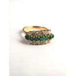 An 18ct gold emerald and diamond three line ring. central line of seven round cut emeralds with