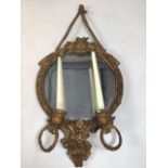 A gesso and gilt decorative circular mirror with candle sconces.