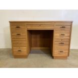A mid century light oak pedestal desk with large central drawer flanked by four pedestal drawers.