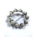 An unmarked precious white metal Bellepoque wreath brooch set with a surround of pearls and