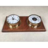 A brass barometer and clock on wooden wall mount.