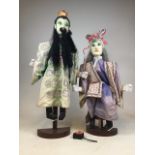 Two large wooden South Asian puppets on wooden plinths. H:105cm and H:90cm