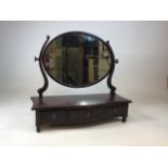 An early 20th century serpentine fronted oval dressing table mirror with three vanity drawers to