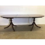 A twin pedestal mahogany dining table with reeded edge with extra leaf, brass feet and castors. W: