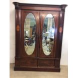 An mahogany Edwardian inlaid double wardrobe with oval bevelled mirrored doors two drawers to base.