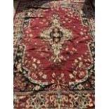 A large red, cream, black and blue modern carpet with large central medallion. W:325cm x H:236cm