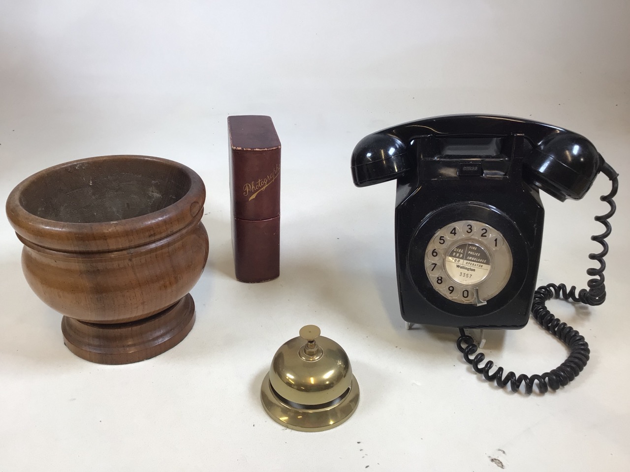 A wall mounted vintage phone, a desk bell, a treen vessel and a book shaped photograph box