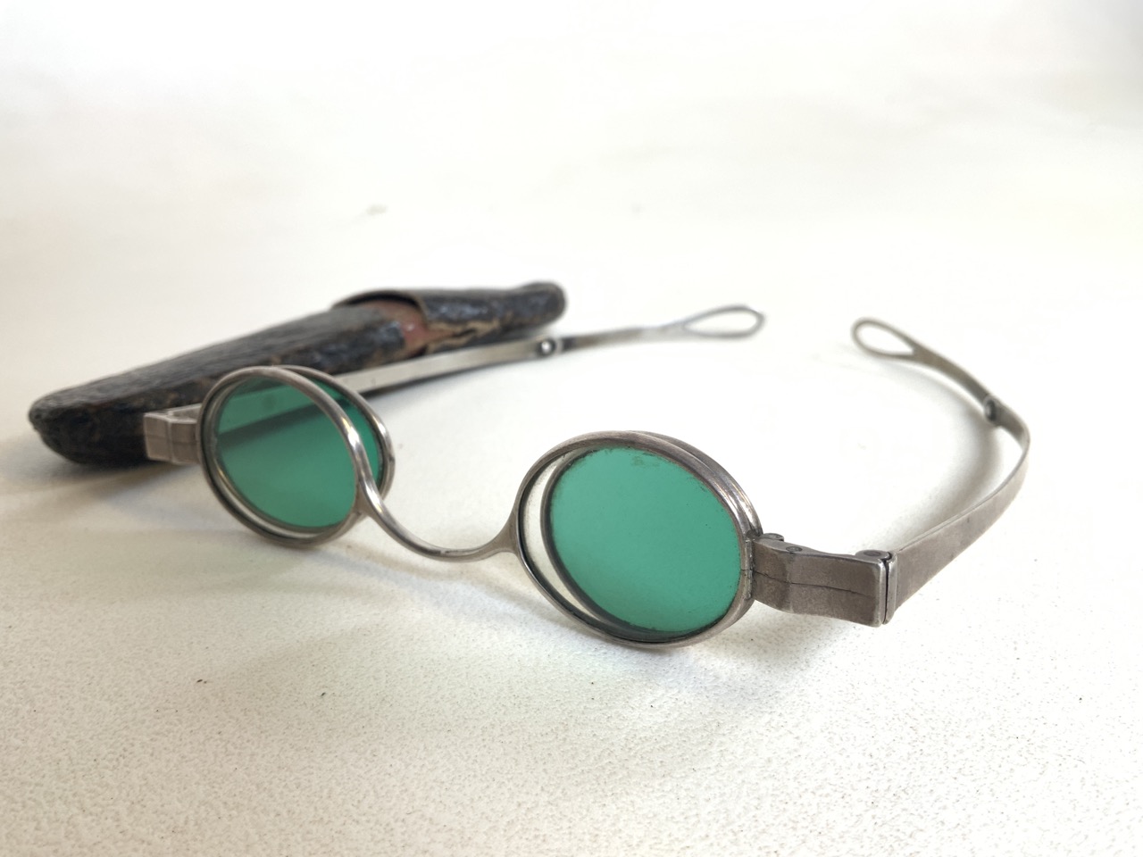 A pair of white metal framed oval lens sunglasses with green and clear glass lenses.