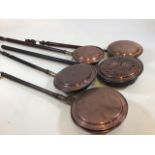 A collection of five copper warming pans.