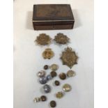 Four metal cap badges together with a collection of military buttons in a carved wooden box