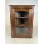 A small early 20th century glazed oak corner cupboard with two fitted shaped shelves, with key.