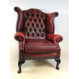 An oxblood red leather Chesterfield style wing back arm chair. W:83cm x D:90cm x H:112cm