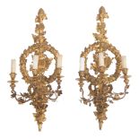A pair of Baroque style carved and gilt wooden wall lights with floral decorated brass arms, richly