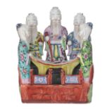 A Chinese famille rose porcelain group depicting five standing sages reading a scroll in a fenced ga