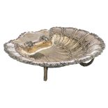 A silver shell-shaped compote on three dolphin-shaped feet, with floral decoration and a ribbon-shap