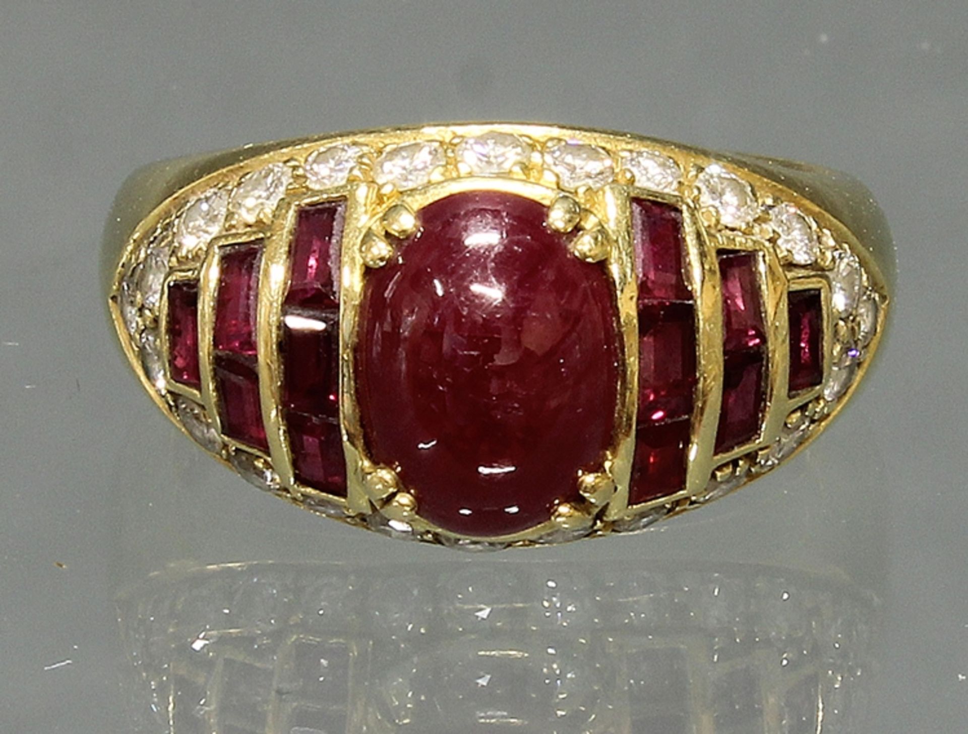 Ring, GG 750, 1 ovaler Rubin-Cabochon, 12 rechteckig facettierte Rubine, 24 kleine Besatzdiamanten,