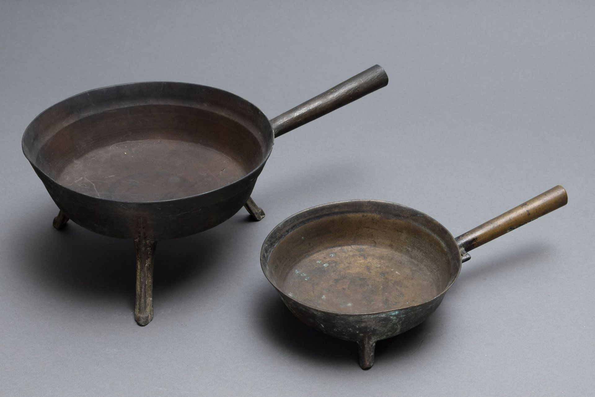2 Diverse Dreifußpfannen mit glattem Stiel, Bronze, wohl 16./17.Jh., H. 6./12cm, Ø 16,5/22cm, Druck