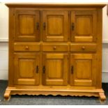 A large country light oak housekeepers cupboard; three fielded panel doors over three drawers, three