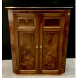 An early 19th century flame Mahogany wall hanging corner cupboard, two paneled doors, shaped