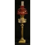 An early 20th century oil lamp, brass Corinthian column, clear glass reservoir, cranberry glass