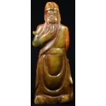 A Chinese soapstone figure, carved as an Immortal, he stands, stroking his beard, 20.5cm high