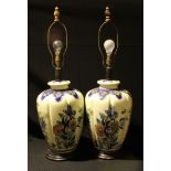 A pair of large lobed ovoid Delft style lamp bases, painted with leafy foliage, ebonised circular
