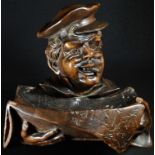 A Black Forest novelty desk tidy, carved as a newspaper vendor, wearing a cap and smoking a cigar,