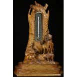 A Black Forest table top thermometer, carved with a Tyrolean shepherd and his flock, 24cm high, c.