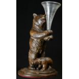 A Black Forest novelty posy vase, as a bear holding a clear glass epergne flute, a cub at her