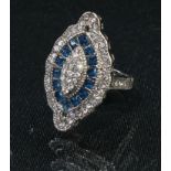 An Art Deco style base metal navette shaped dress ring, set with an arrangement of clear and blue