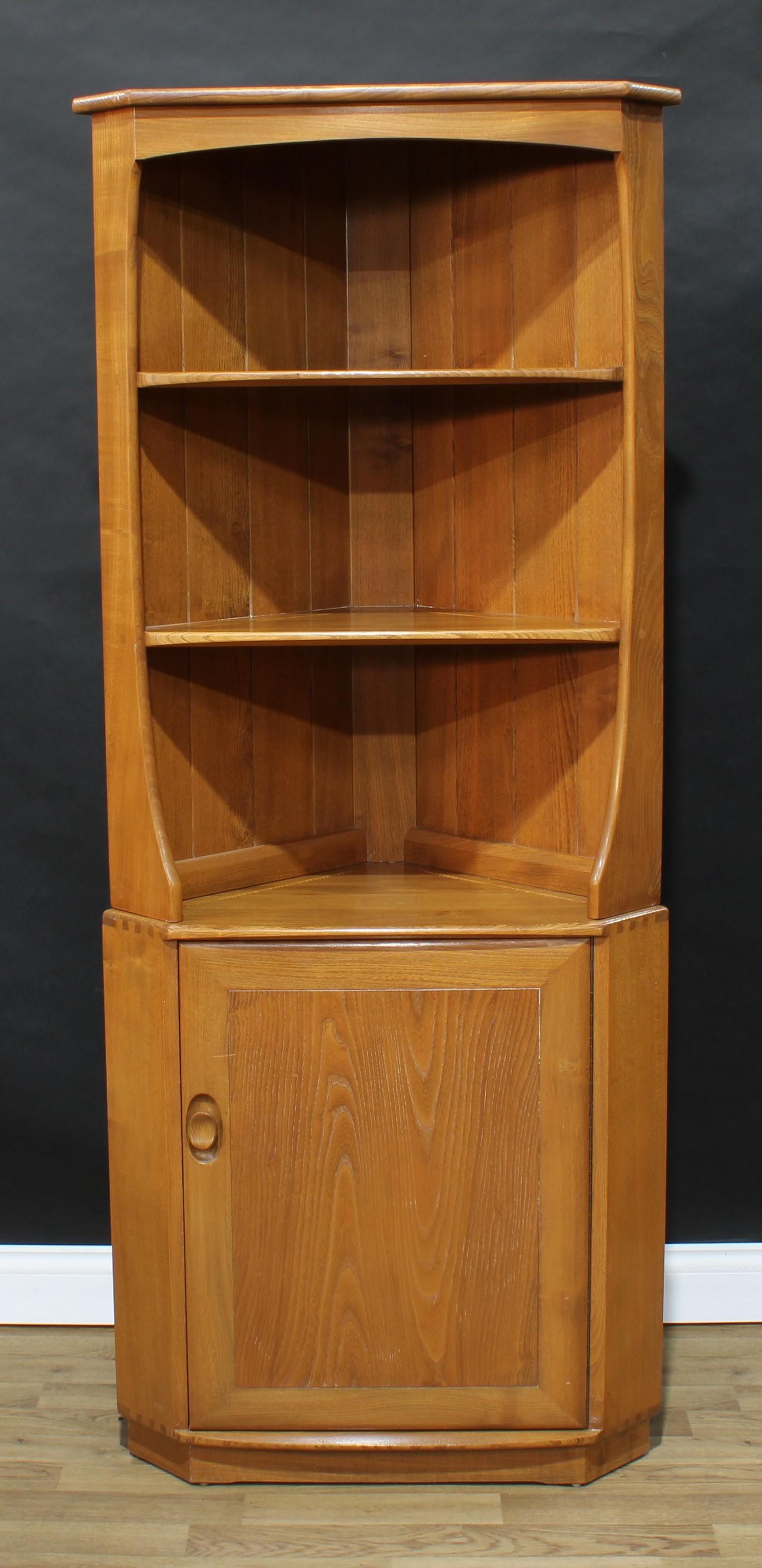 An Ercol elm corner display cabinet, shallow cornice above two open shelves above a door enclosing a