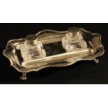 A George V silver shaped rectangular inkstand, the pair of glass inkwells flanked by dished pen