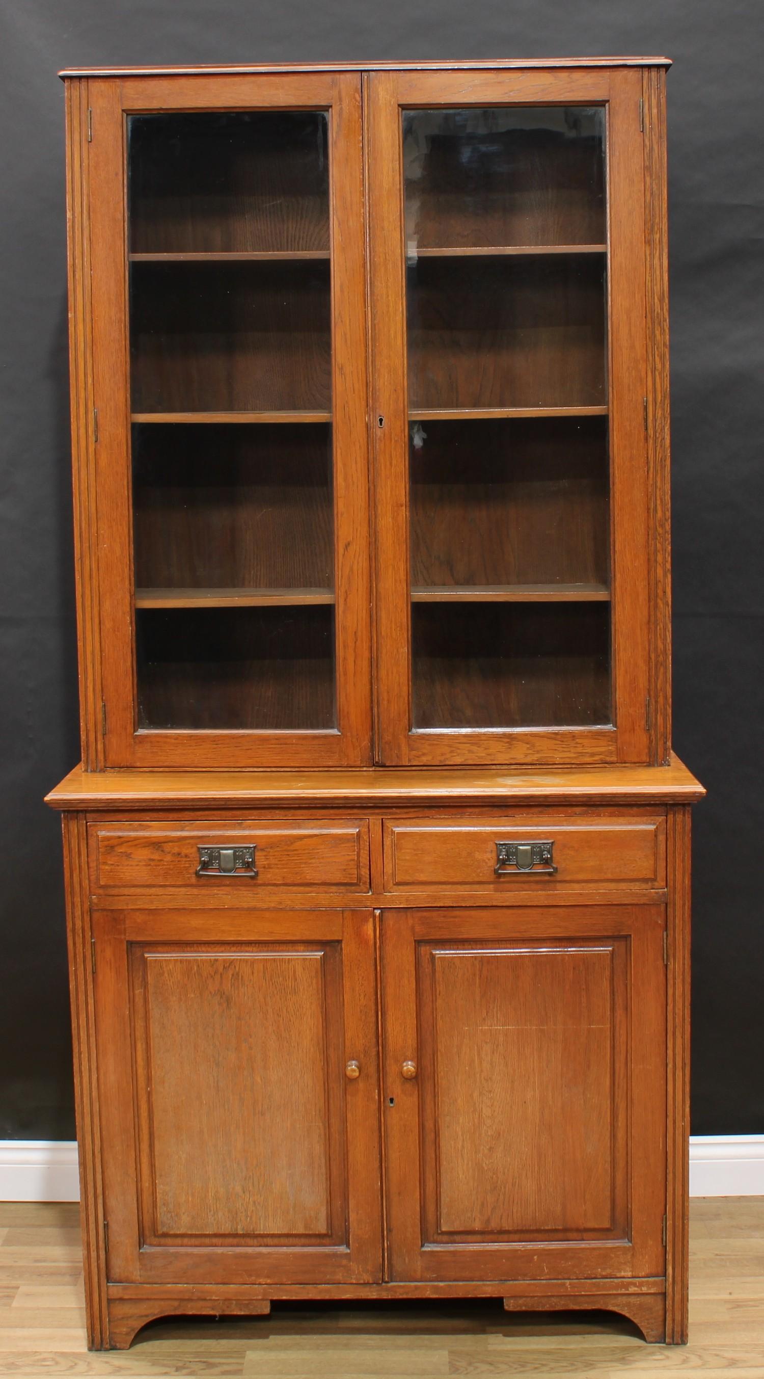 An Arts & Crafts design oak bookcase cabinet, shallow half gallery above a pair of glazed doors