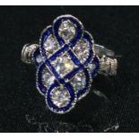 An Art Deco style base metal kite shaped dress ring, set with clear glass and blue enamel, ring size