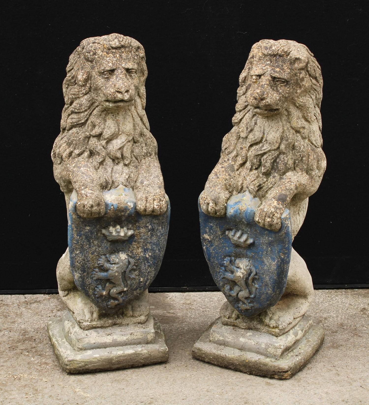 A pair of reconstituted stone heraldic lions, each grasping a shield, stepped bases, 74cm high, 26cm