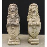 A pair of reconstituted stone heraldic lions, each grasping a shield, stepped bases, 81cm high, 26cm