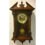 A walnut wall clock, architectural pediment, brass dial, enamelled chapter ring, Roman numerals.