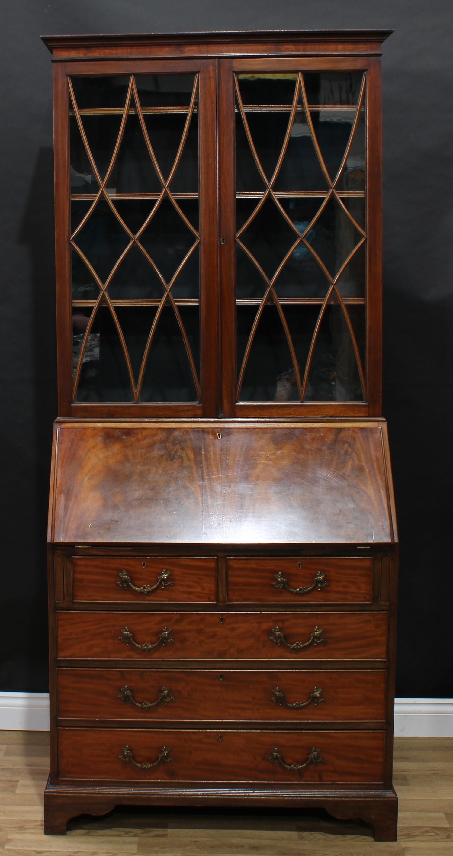 A George III Revival mahogany bureau bookcase, shallow outswept cornice above a pair of glazed doors