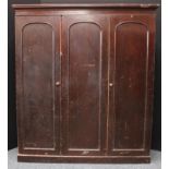 A late Victorian stained pine wardrobe press, outswept cornice above three panel doors, the left