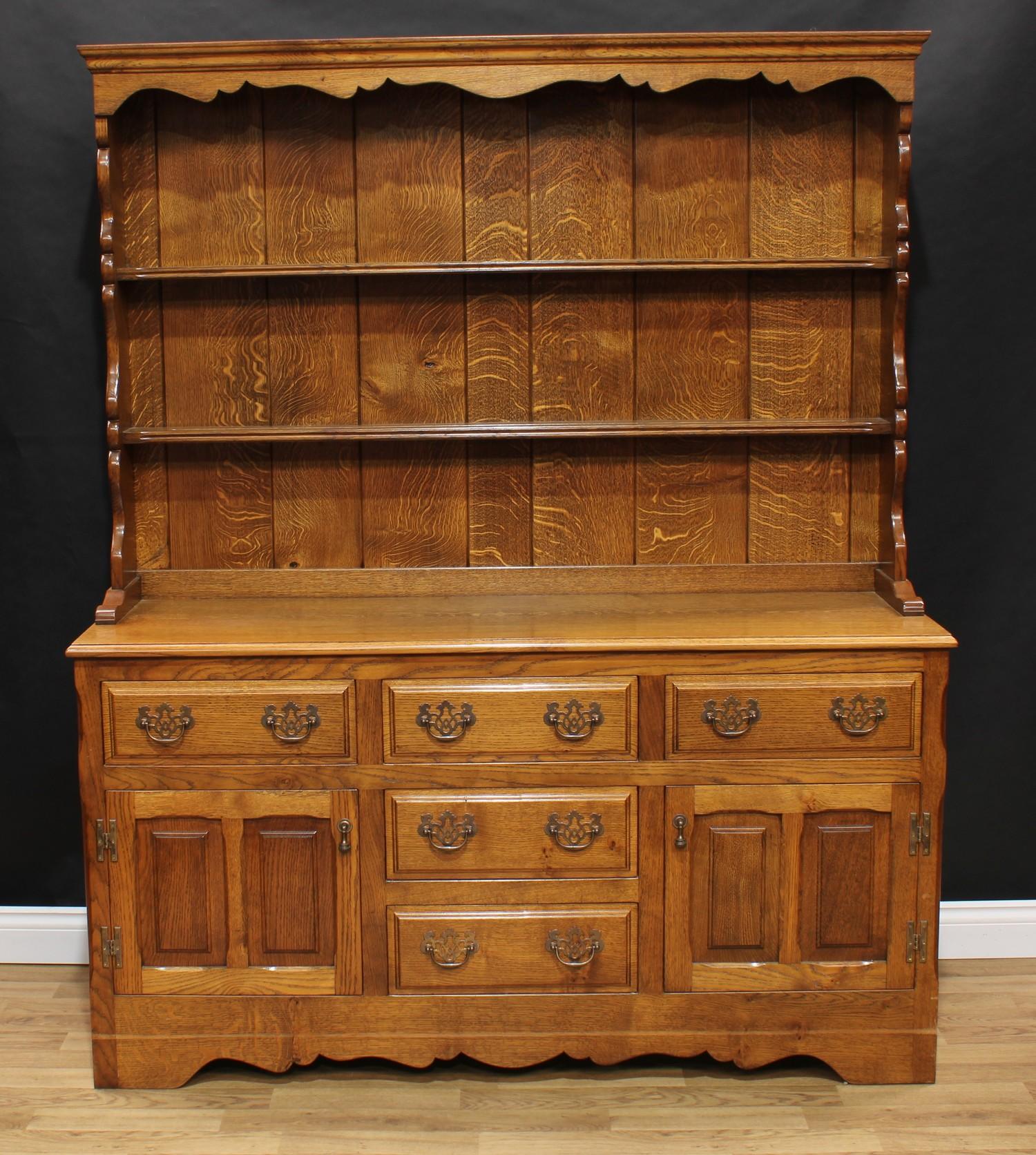 A George III style oak dresser, outswept cornice above a shaped apron and two plate racks, the