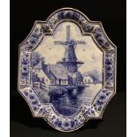 A Delft Blauw shaped oval dish/plaque, painted with riverside windmill, 35cm x 27.5cm