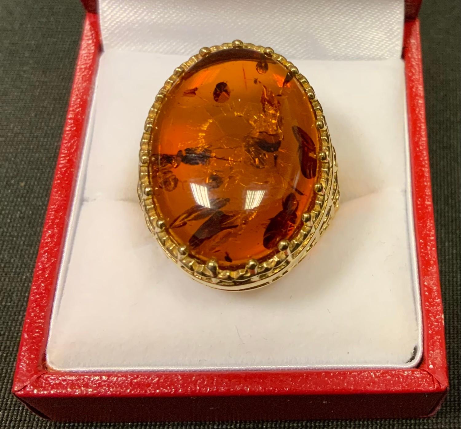 A large yellow metal dress ring mounted with an oval baltic amber cabochon , insect wing inclusions,