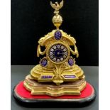 A gilt metal mantel clock under a glass dome, eagle and globe finial, blue enamelled face,