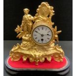 A gilt metal figural mantel clock under a glass dome, man with tricorn hat stands to one side,